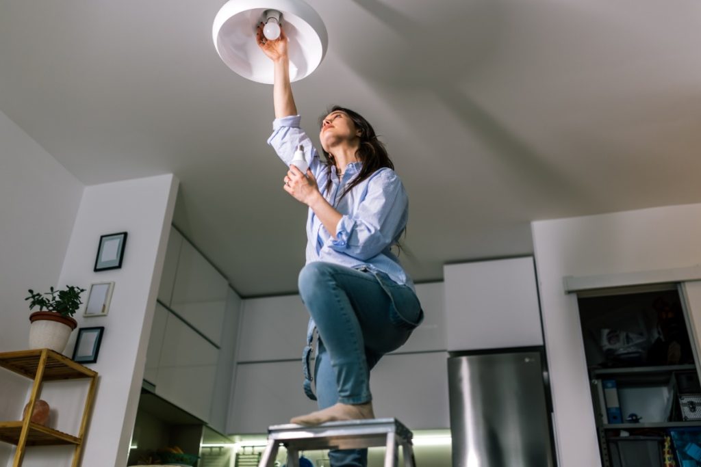 Homeowner tightening a loose light bulb during basic home maintenance