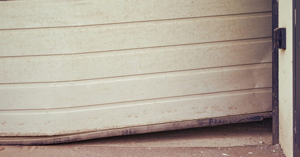 Garage door with bent panel and off-track damage from storm winds.