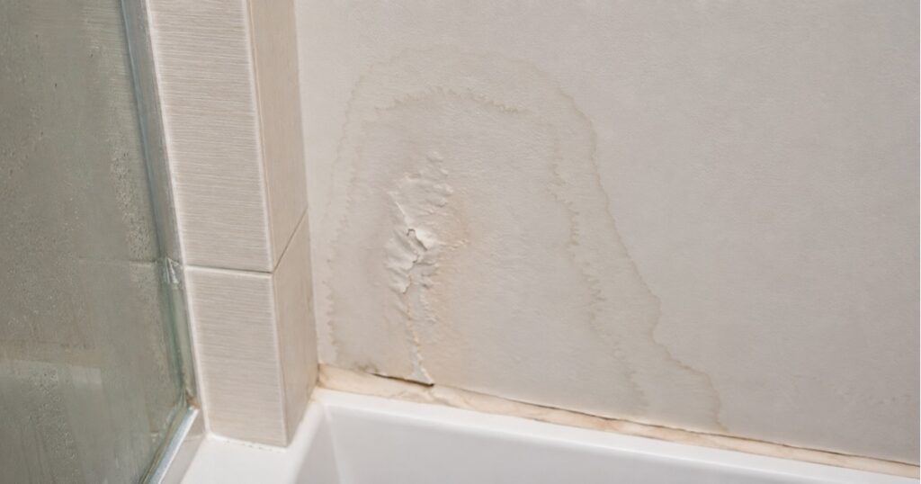 Water stain and soft drywall spot near a bathroom shower wall