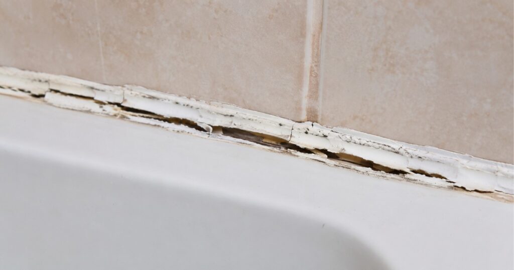 Cracked and peeling caulk along the edge of a bathroom bathtub