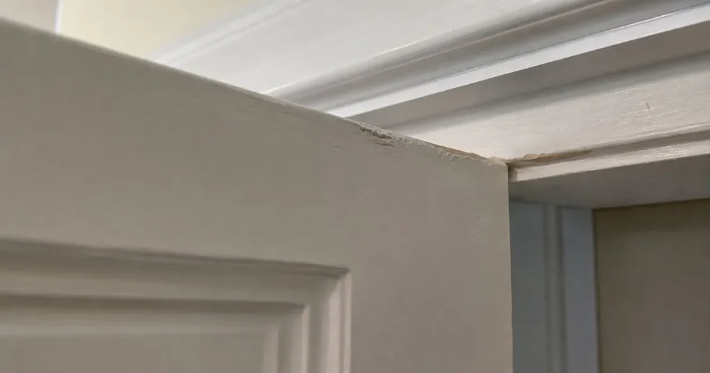 Close-up of the top edge of a wood door rubbing against the door jamb