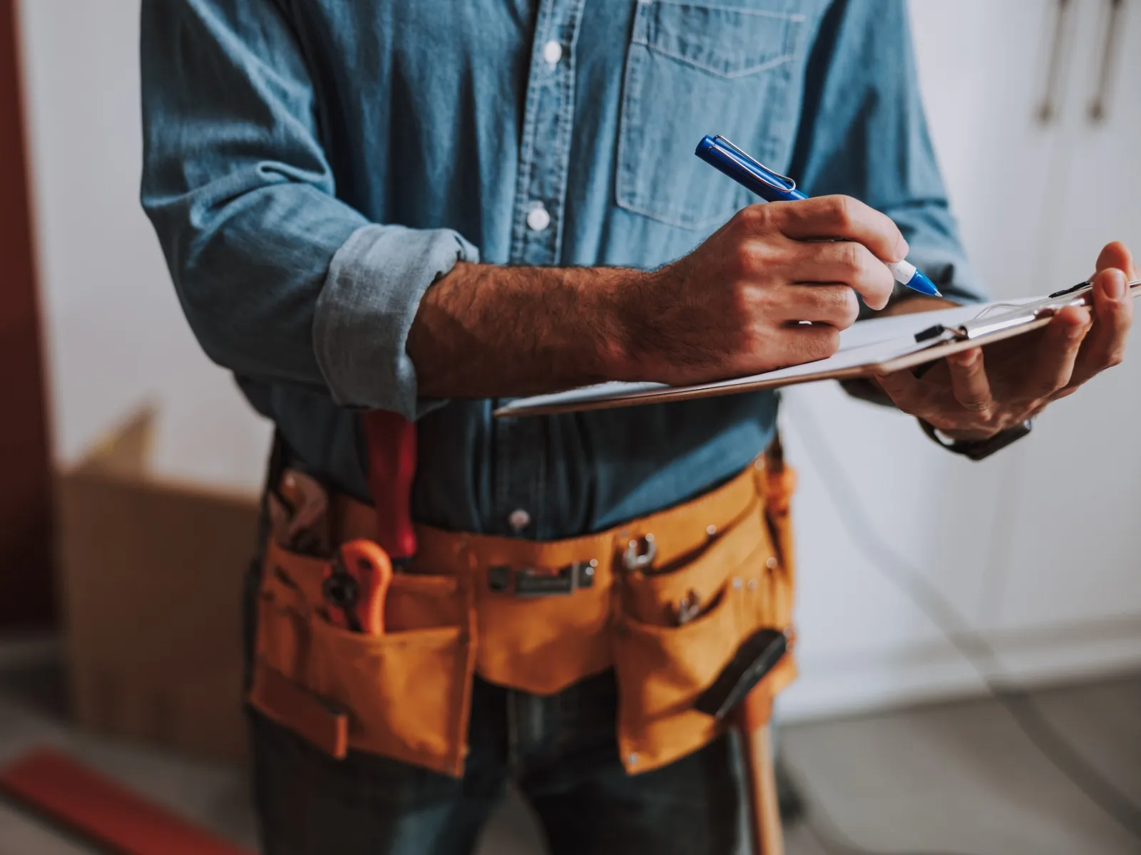 Handyman wearing a tool belt and writing on a clipboard