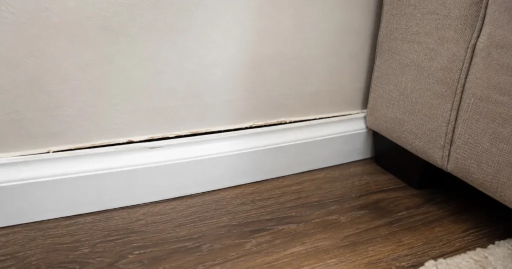Baseboard trim separating from a living room wall with a visible gap