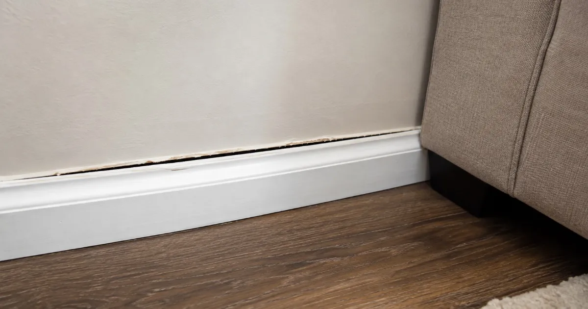 Baseboard trim separating from a living room wall with a visible gap